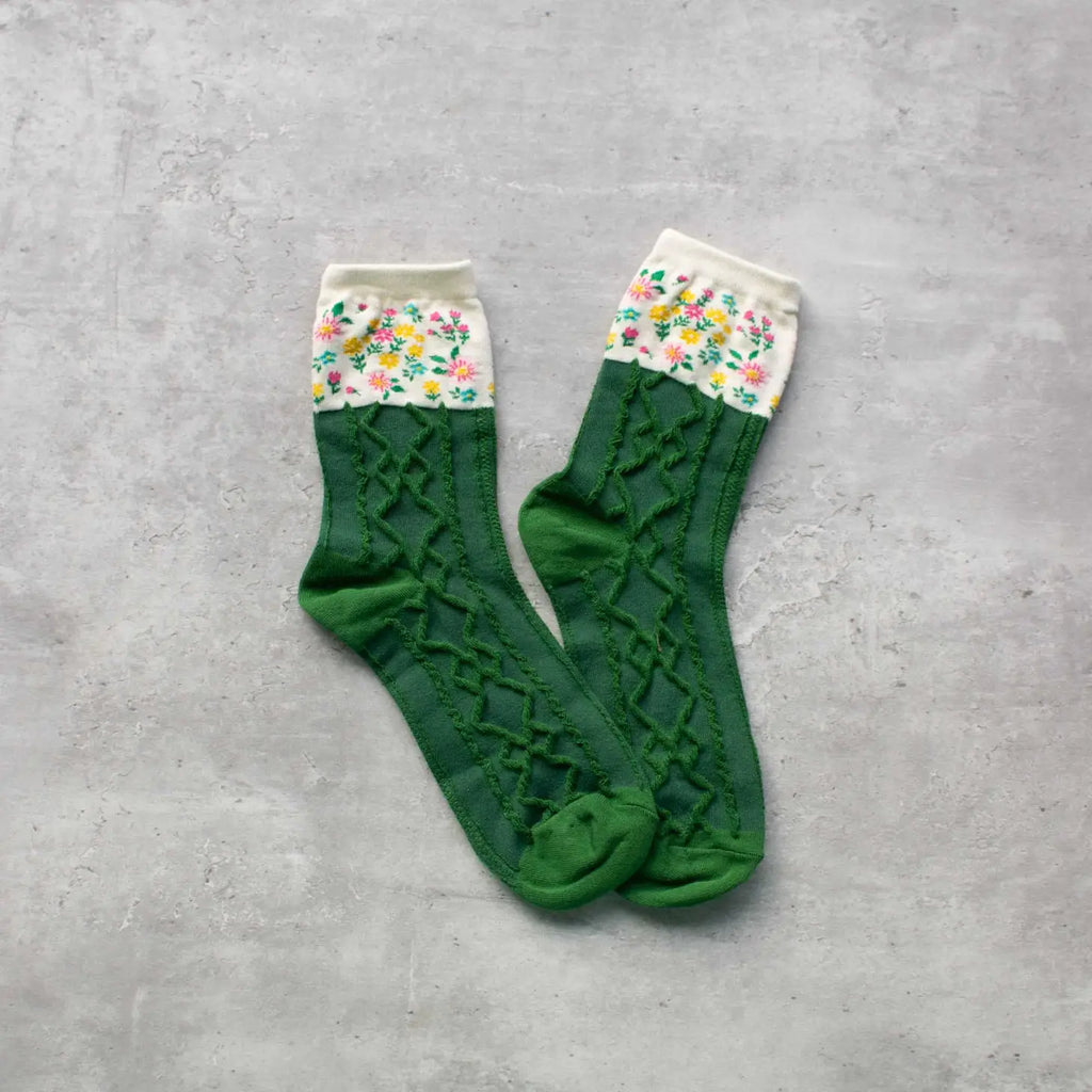 A pair of green socks with a floral pattern on the cuffs placed on a gray background.