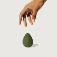 A hand reaching towards a green egg-shaped object on a plain background.