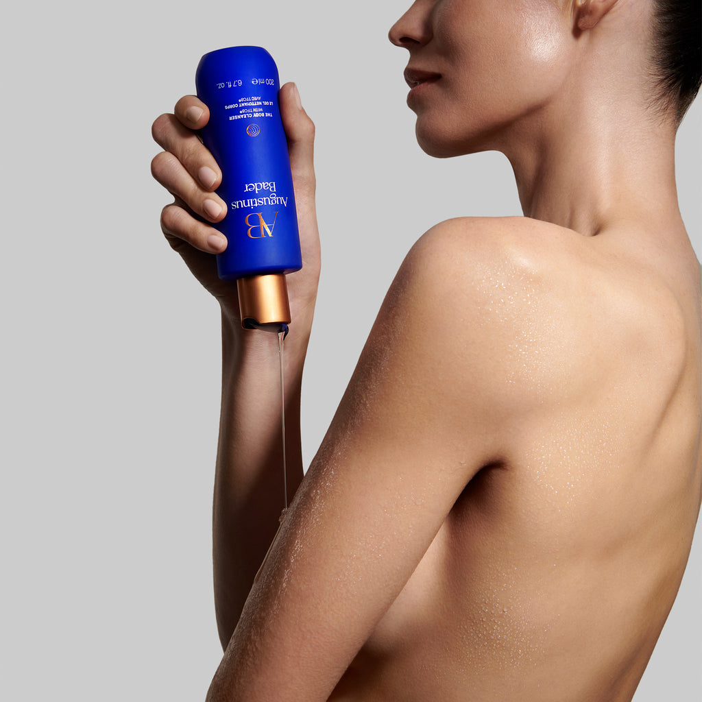 A person holding a blue bottle of skincare lotion, with moisturized skin visible.