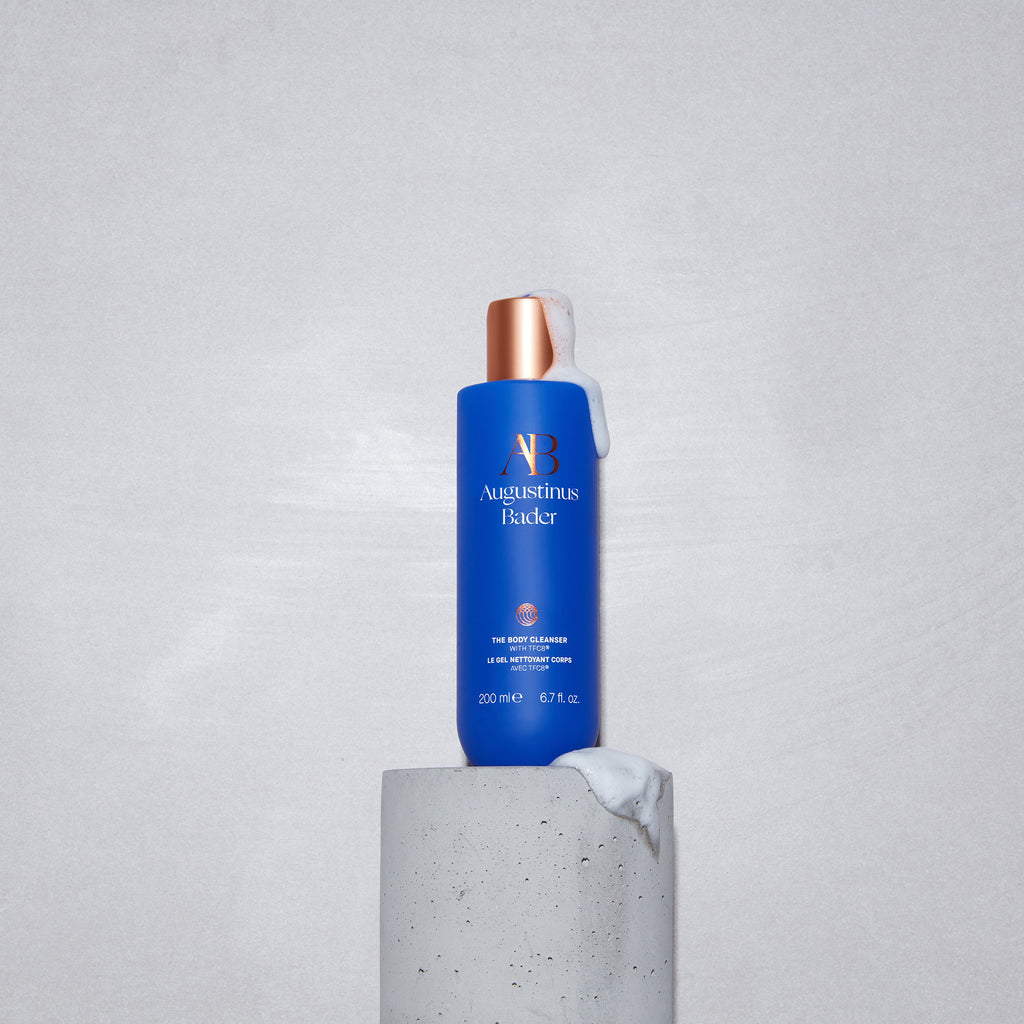 A bottle of augustinus bader skincare cream displayed on a gray stone pedestal against a simple background.