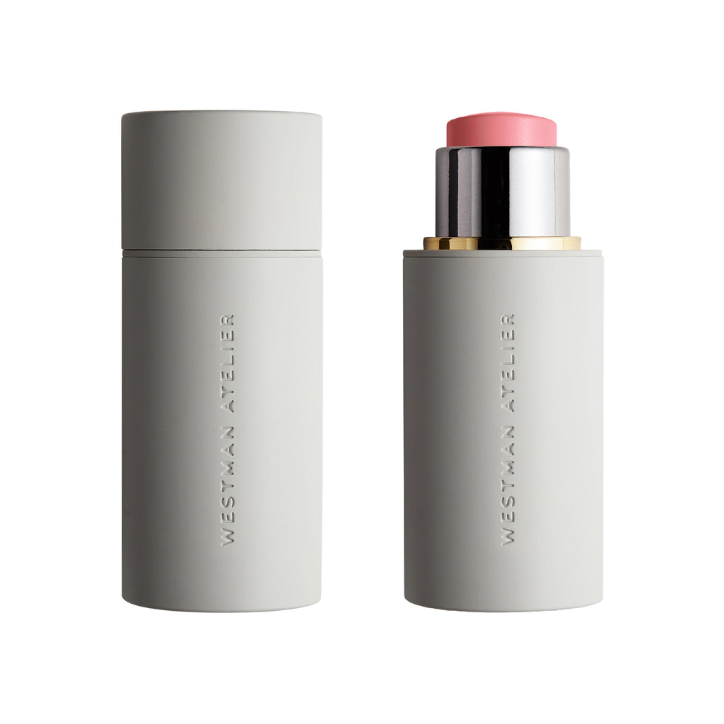 A Westman Atelier Baby Cheeks Blush Stick in a gray tube, with the lid off to reveal a pink-toned product with buildable color.