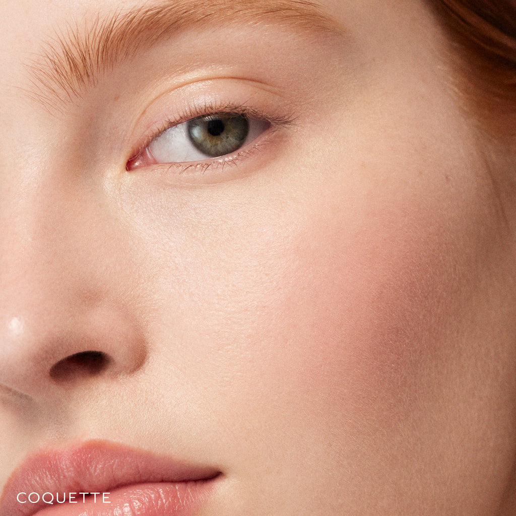 Close-up of a woman's face focusing on her green eye, fair skin, and light brown eyebrow created with Westman Atelier Baby Cheeks Blush Stick, with part of her nose and lips visible.
