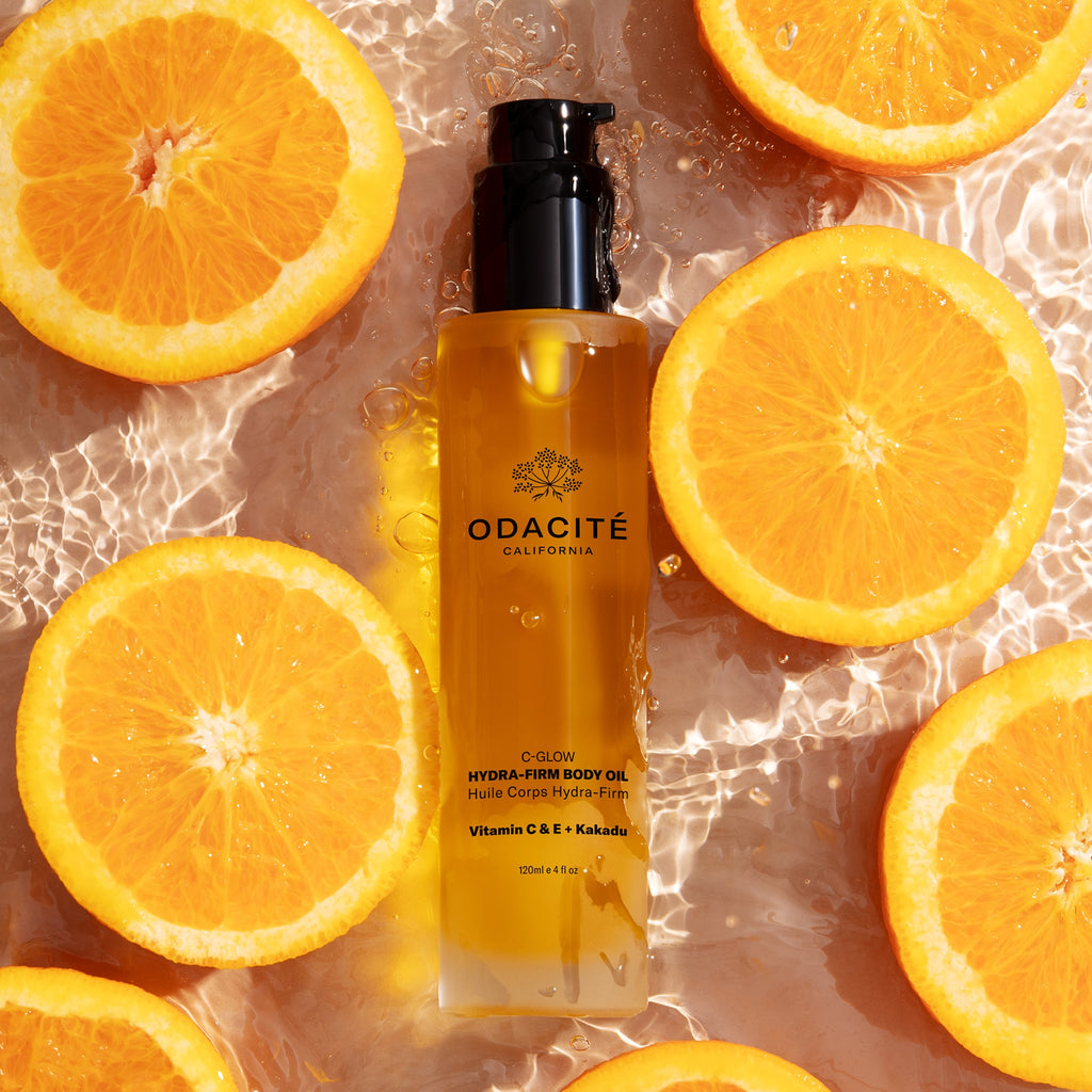 Bottle of odacite body oil surrounded by fresh orange slices on a watery surface.