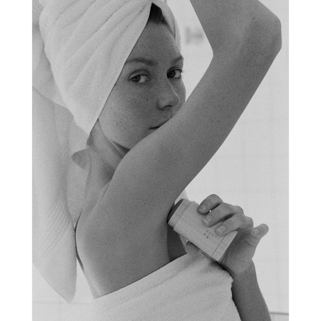 Black & White photo of a female model wearing a towel on her body and head applying corpus deodorant