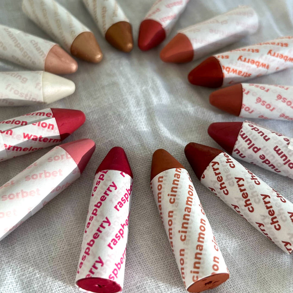 Assorted lipsticks with fruit names scattered on a textured surface.