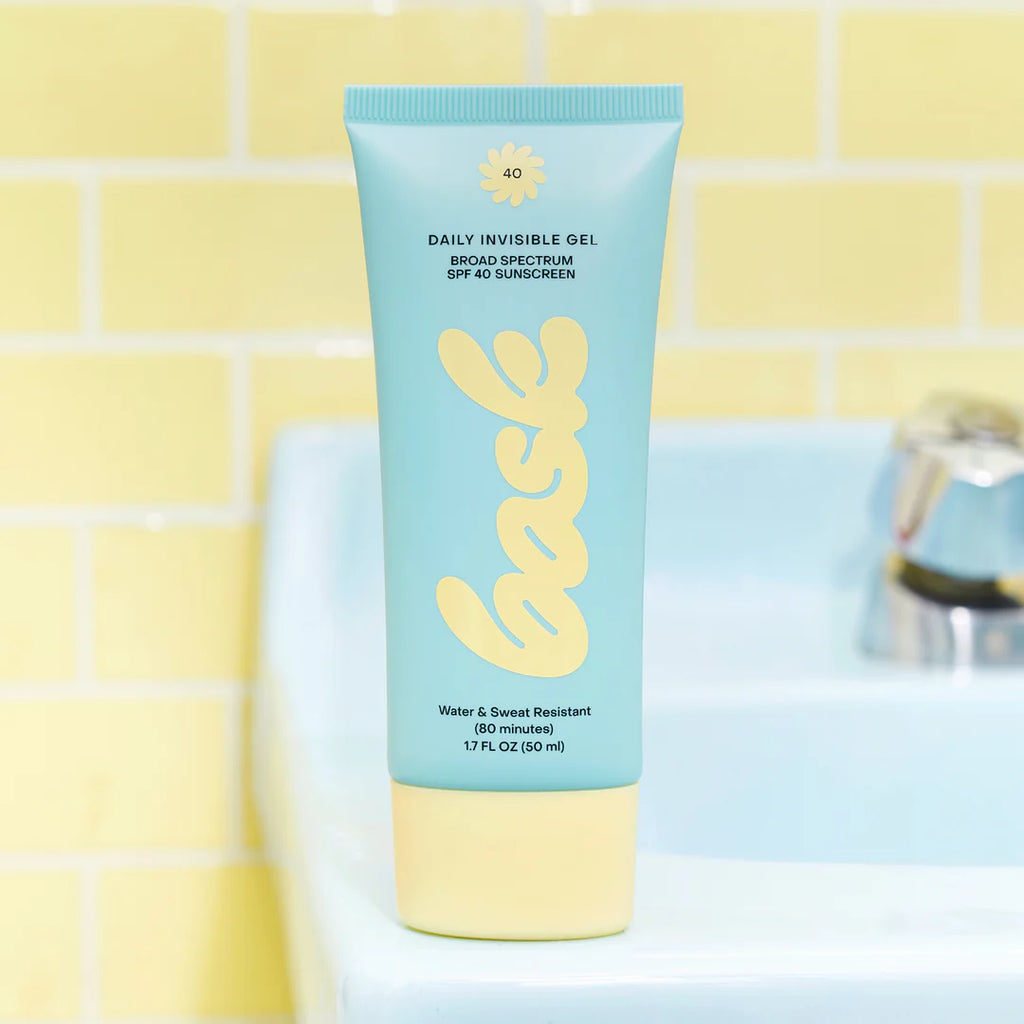 Bask Daily Invisible Gel SPF 40 tube standing on a bathroom sink with a yellow tile background.