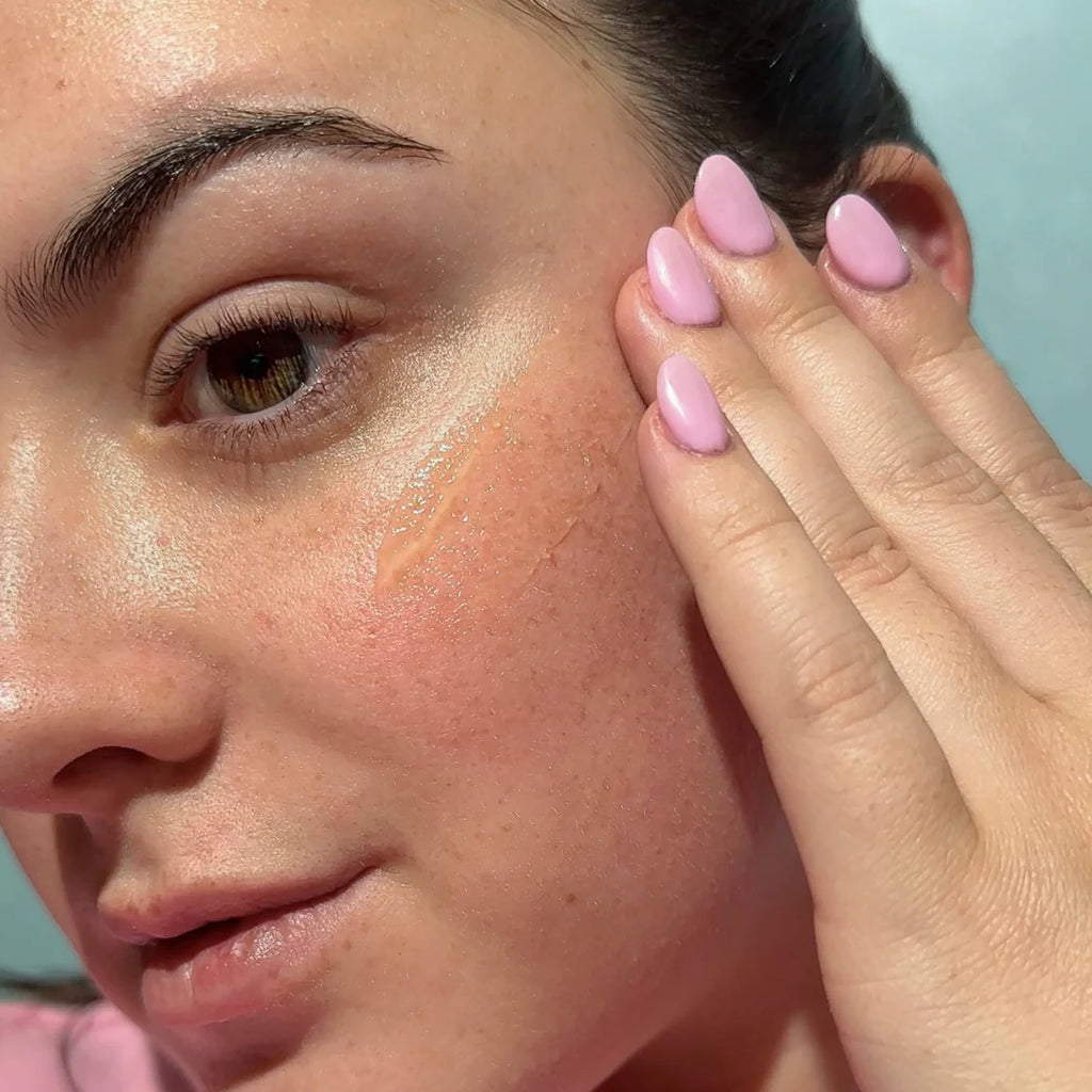 Close-up of a woman's face highlighting her glowing cheek and pink manicured nails, enhanced by her application of Bask Daily Invisible Gel SPF 40 Sunscreen.