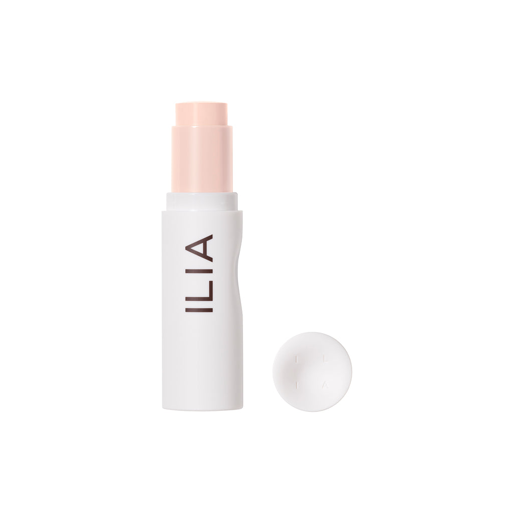 A stick of ilia brand makeup with its cap placed beside it on a white background.