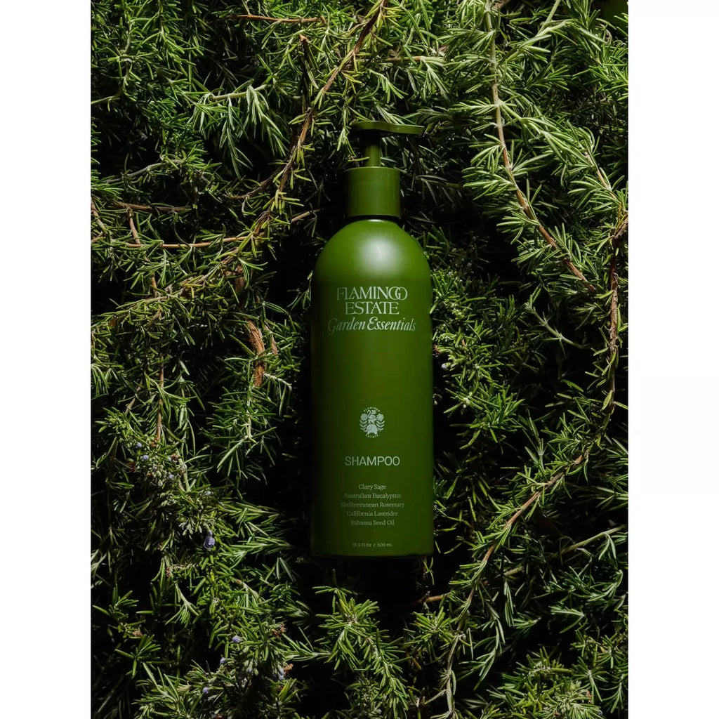 Green shampoo bottle nestled in fresh rosemary herbs.