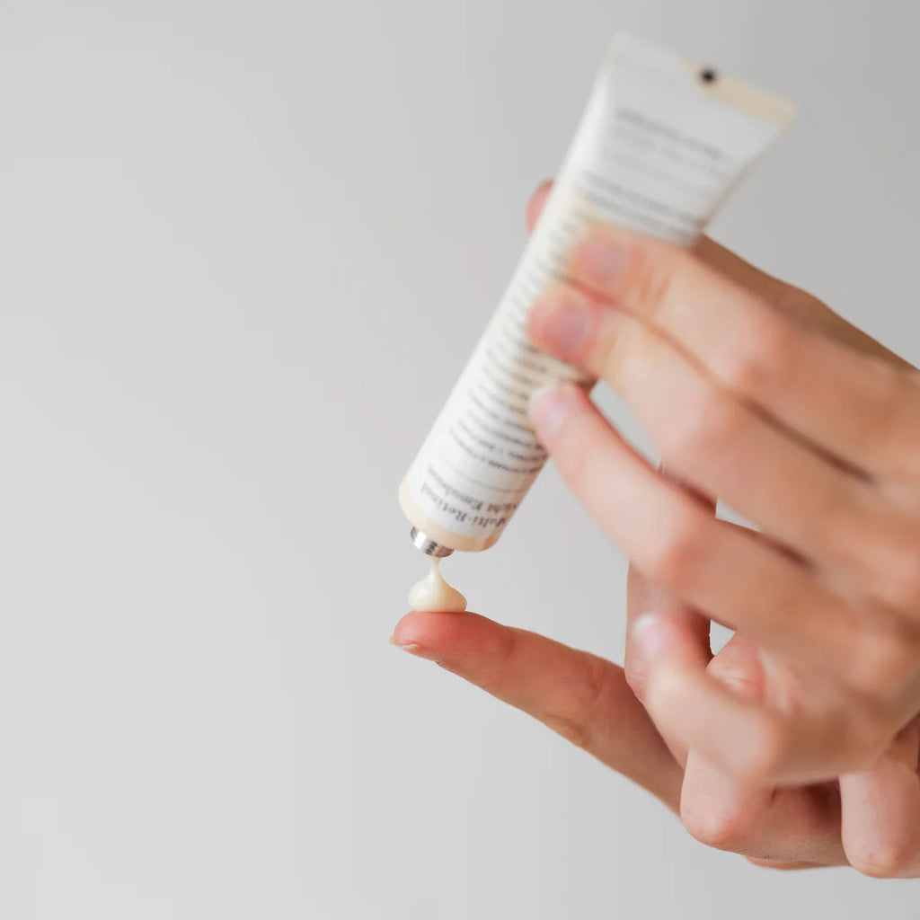 A person squeezing a small amount of cream from a tube onto their finger.