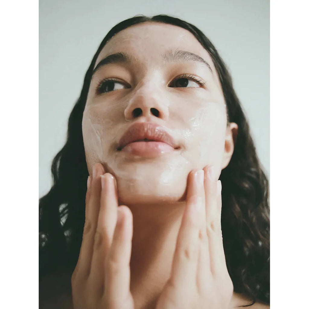 Young woman applying LESSE Calming Cleanser, looking upwards, with hands gently touching her face.