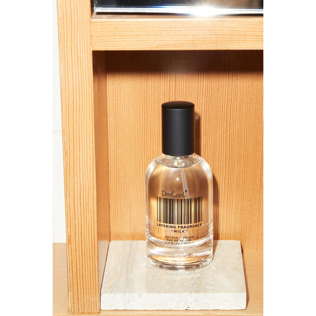 A bottle of dedcool layering fragrance placed on a marble stand against a wooden background.