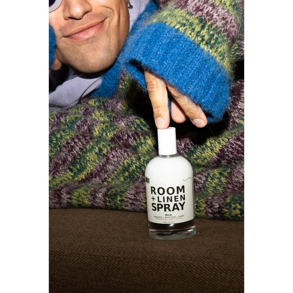 Person holding a bottle of room and linen spray with a content smile.