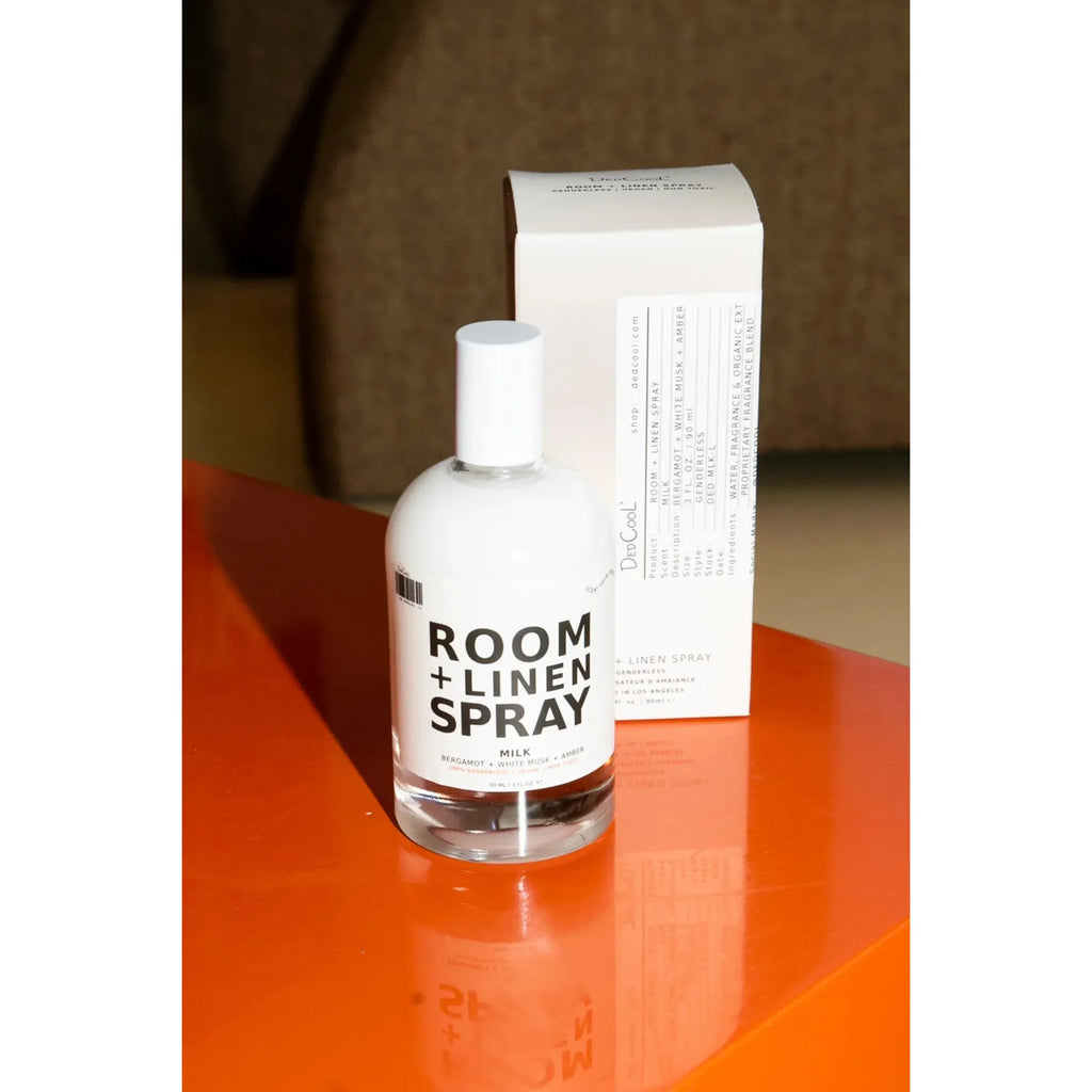 A bottle of room and linen spray with its packaging on a reflective orange surface.