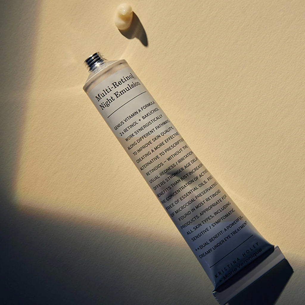 A tube of multi-retinoid night emulsion skincare product with a drop of cream on top, casting a shadow on a plain surface.
