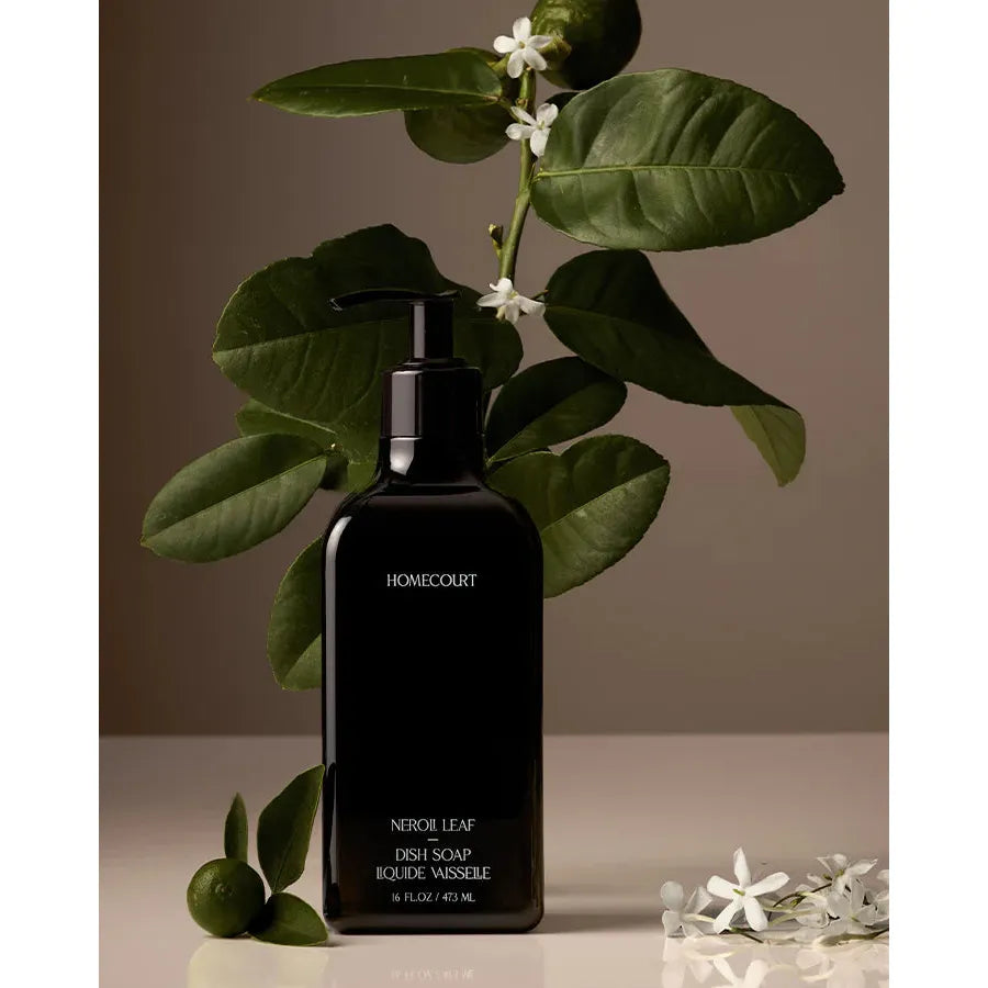 A black bottle of neroli leaf Homecourt Dish Soap labeled "homecourt" with green leaves and white flowers against a beige background.