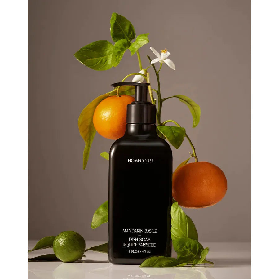Black bottle of Homecourt Dish Soap surrounded by fresh citrus fruits and leaves against a gray background.