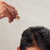 Applying hair oil to the scalp with a dropper.