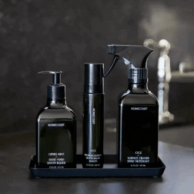 Three sleek black bottles labeled hand wash, hand cream, and surface cleaner in a Homecourt Yamazaki Home Steel Tray, rotating on a dark countertop.