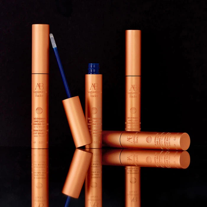 An assortment of copper-toned cosmetic products, including a mascara, artfully displayed against a black background.