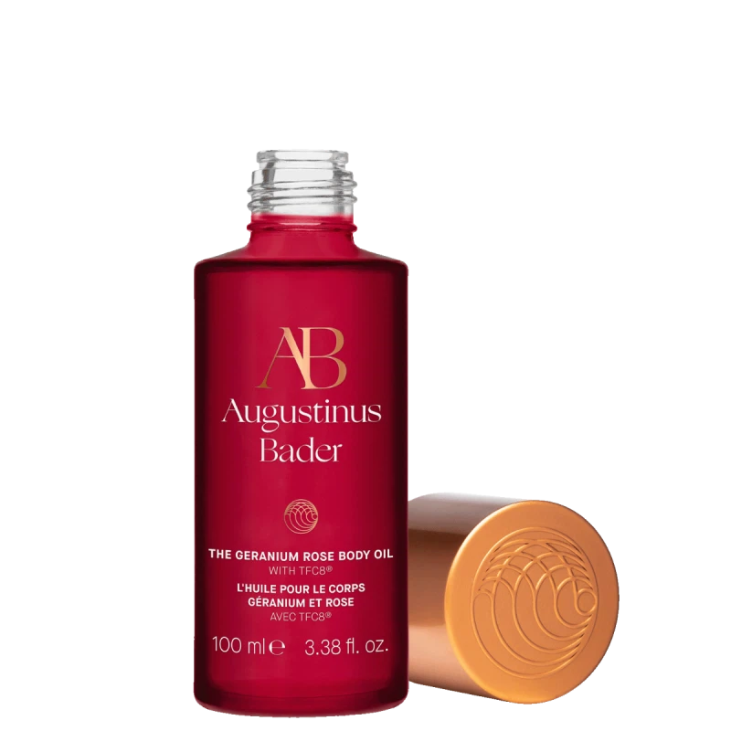 A bottle of augustinus bader the geranium rose body oil with a golden cap beside it.