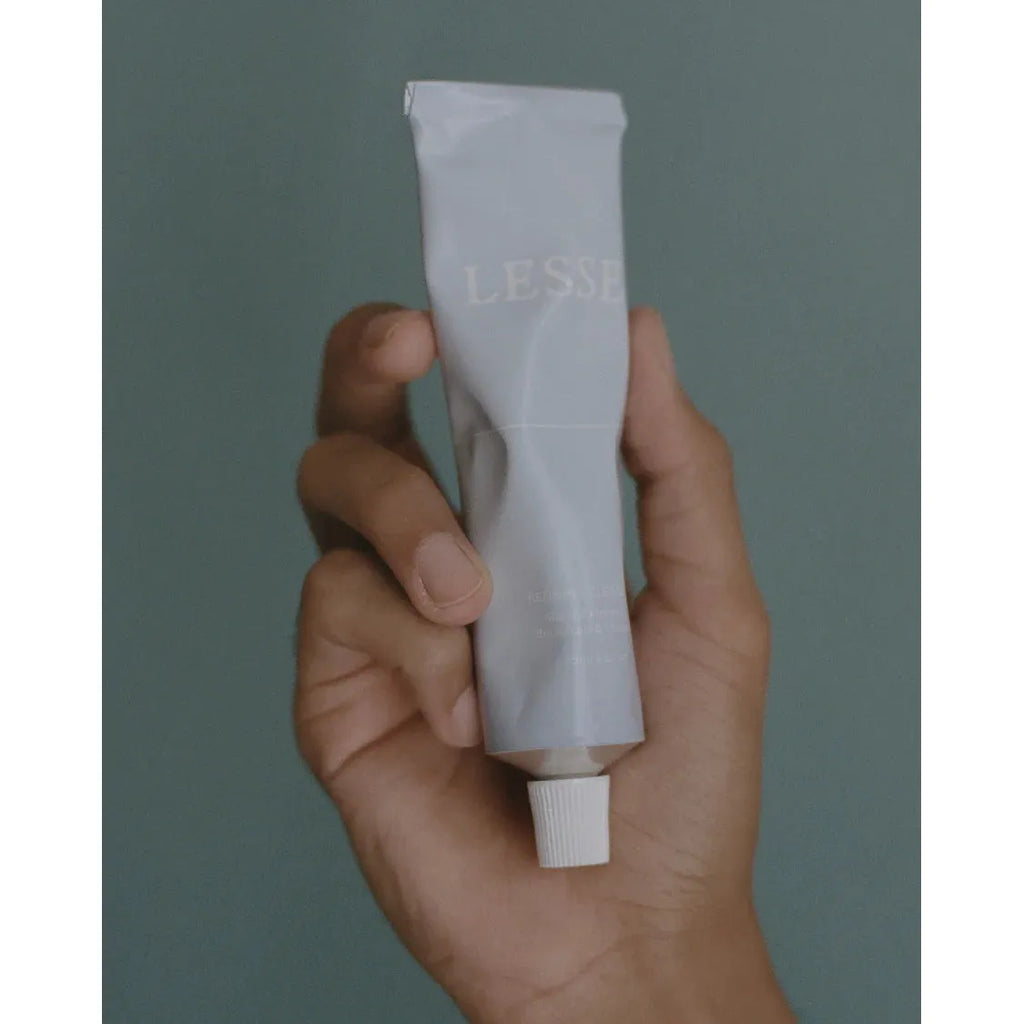 A hand holding a tube of lesse refining cleanser against a teal background.