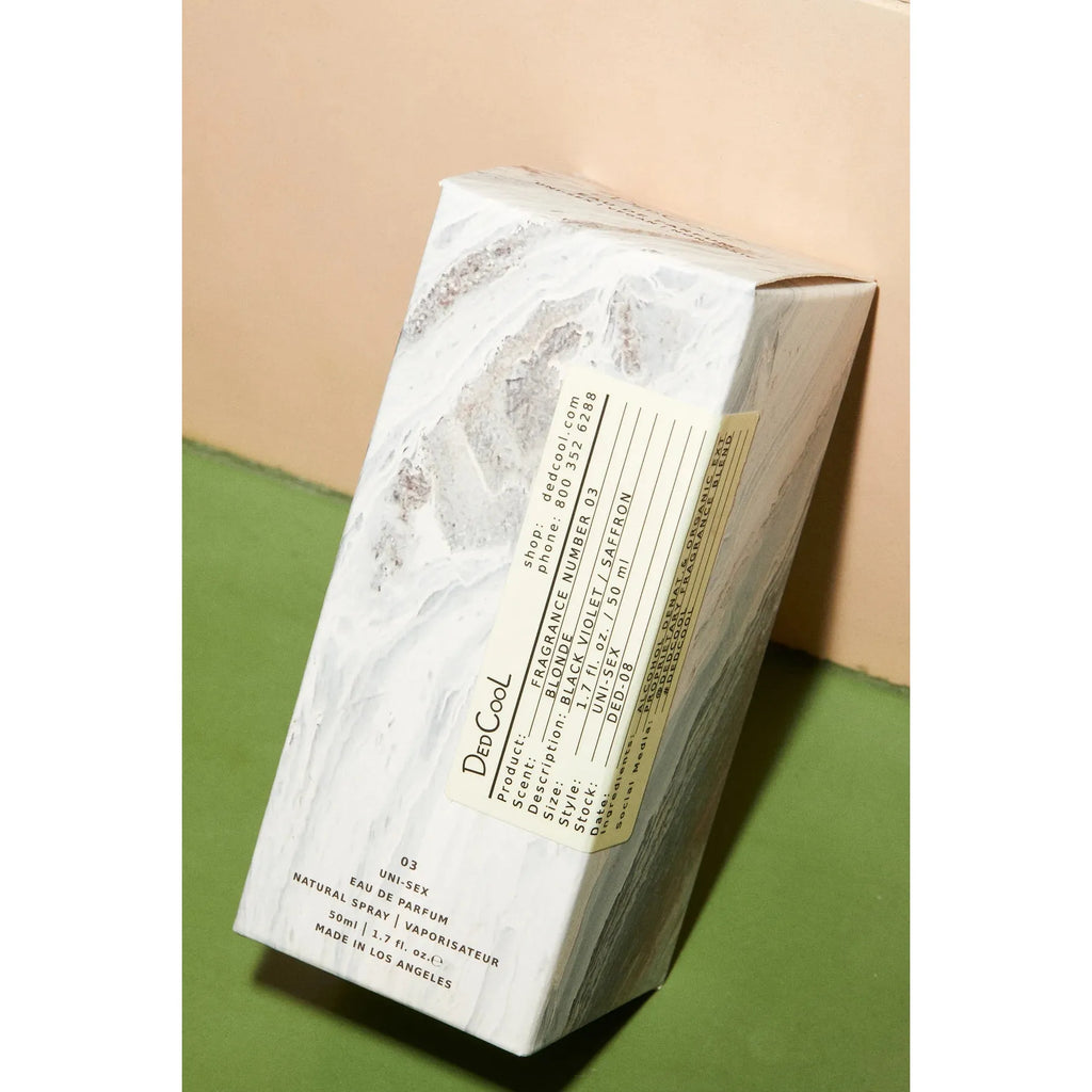 A packaged diptyque candle with a marble design, resting on a tilted two-tone (beige and green) background.