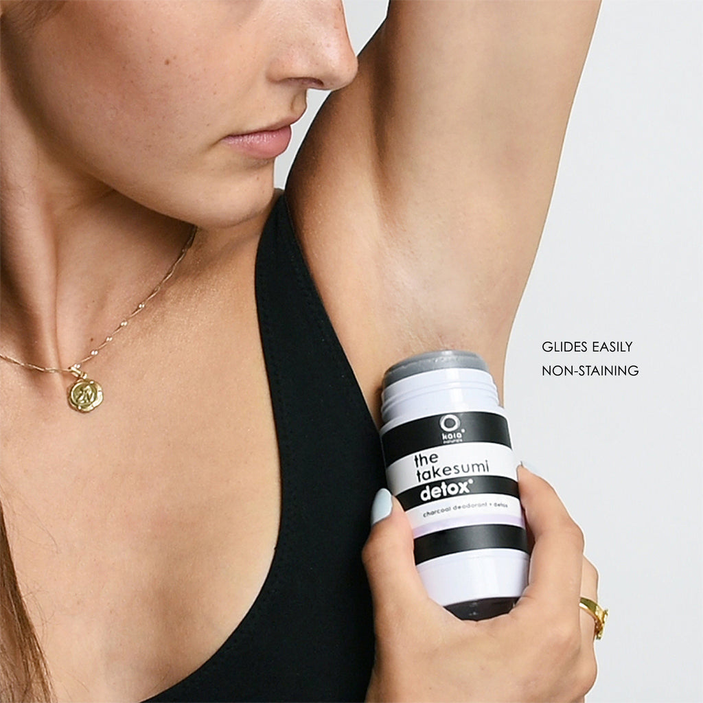 Woman applying roll-on deodorant to underarm.
