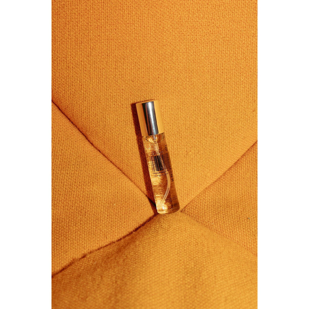 A small perfume roll-on bottle on an orange textured surface.