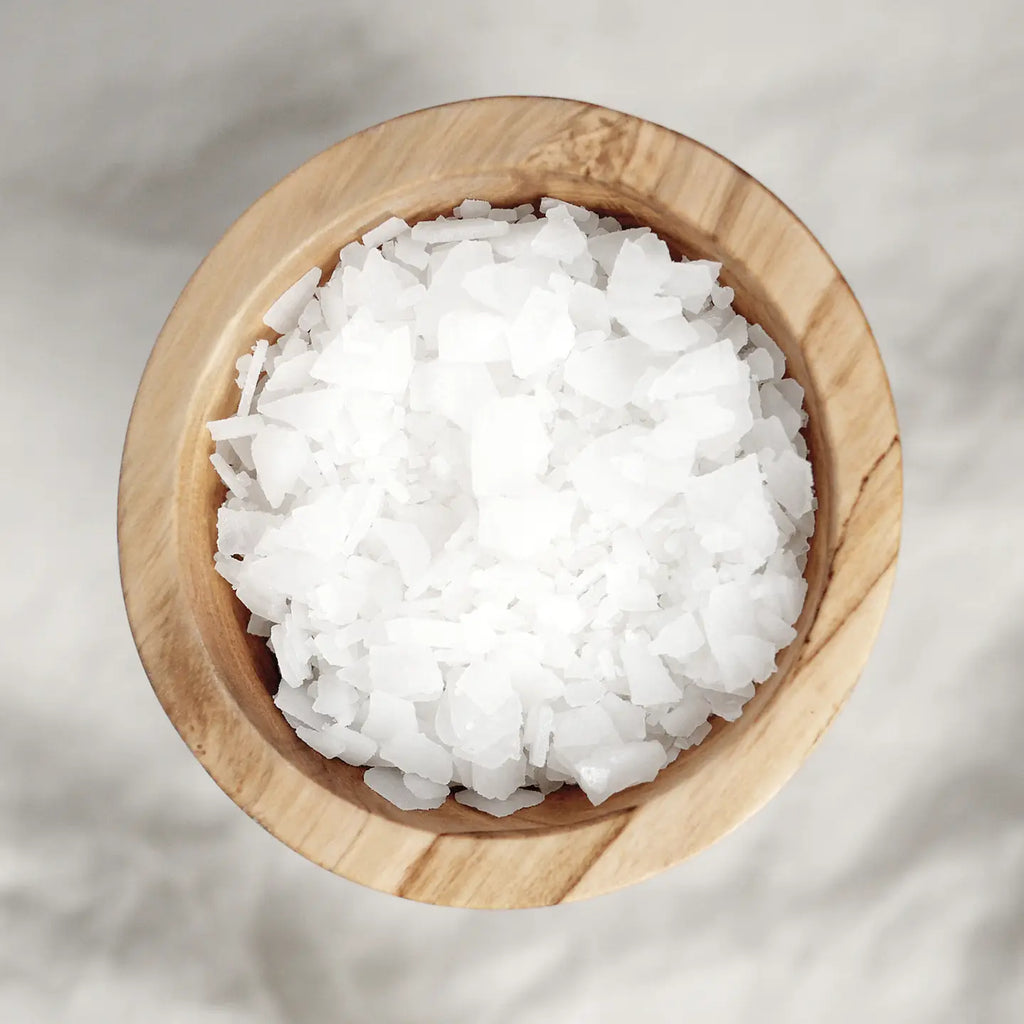 A top-down view of a wooden bowl filled with Mother Mother's Magnesium Bath Soak, featuring coarse sea salt flakes and a hint of lavender essential oil.