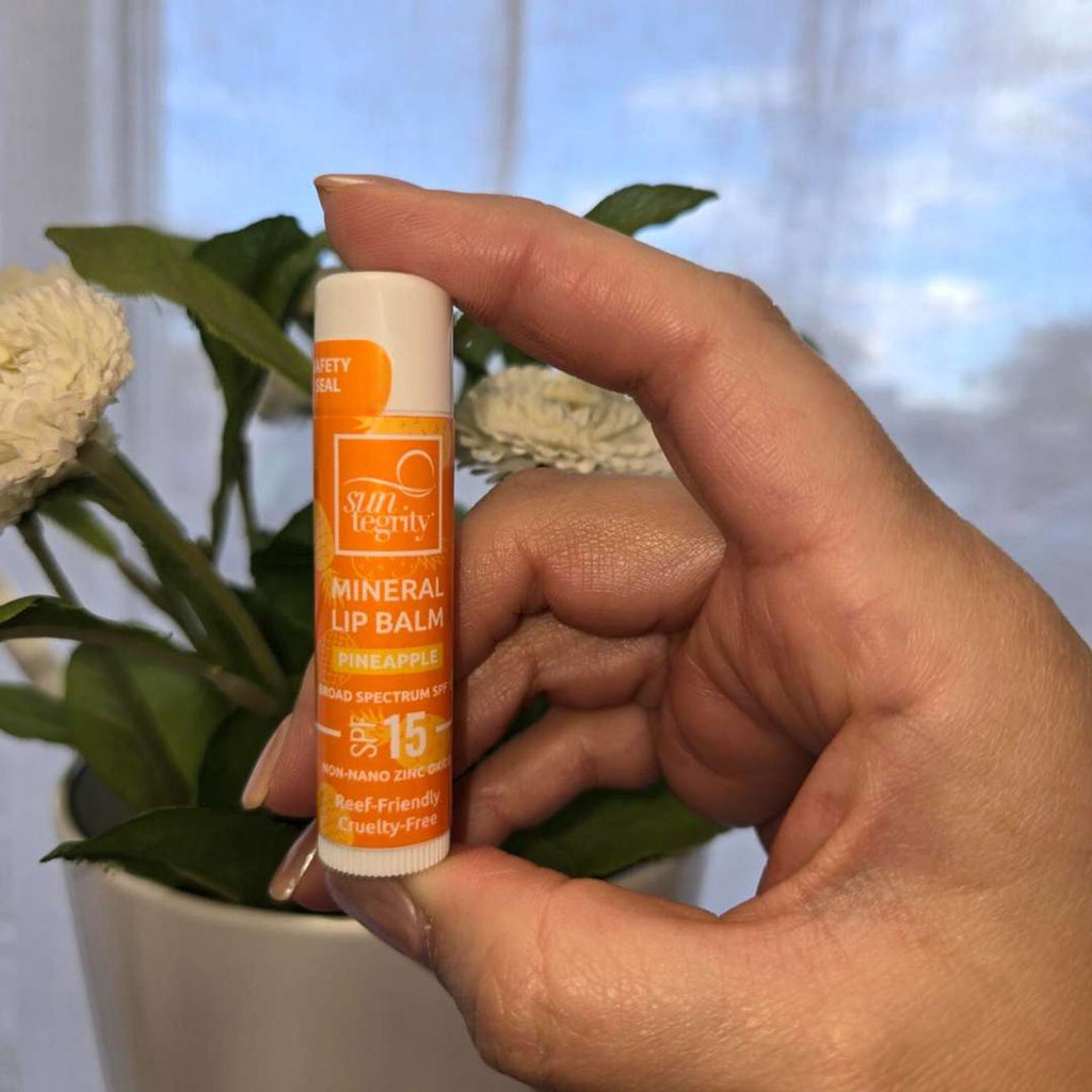 A person holding a tube of mineral lip balm with spf 15 in front of some white flowers.