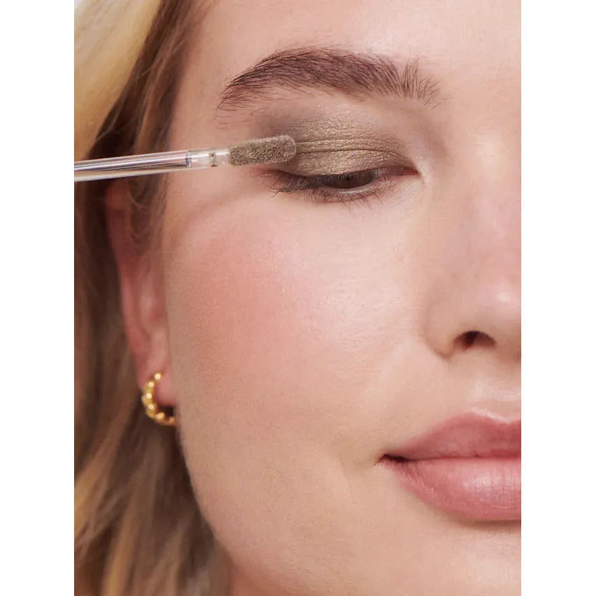 Applying olive green eyeshadow on a woman's eyelid with a brush.