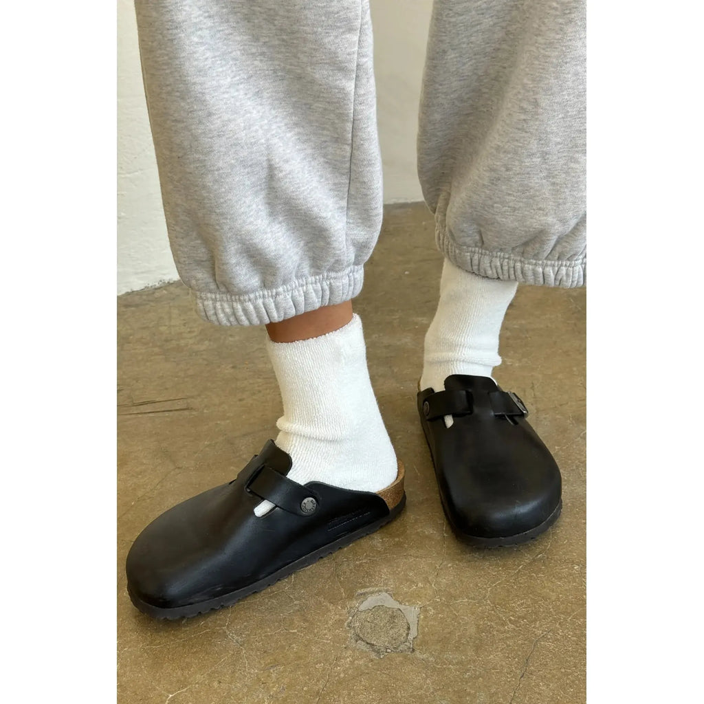 Person wearing white socks and black clogs on a concrete floor.