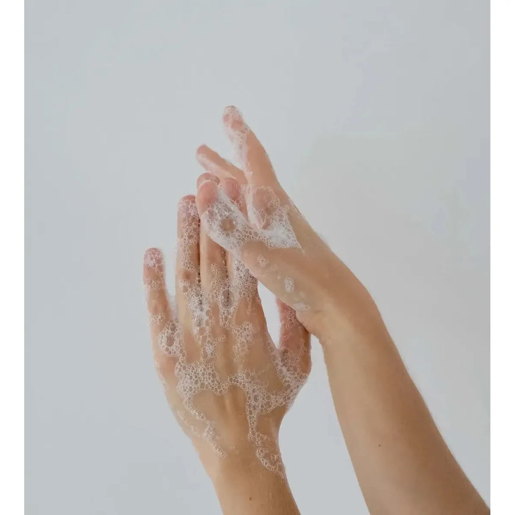 Two hands are shown being washed with the Susanne Kaufmann Hand Soap from the Hand Soap & Hand Lotion Set, with visible bubbles and suds. The background is plain and light-colored.