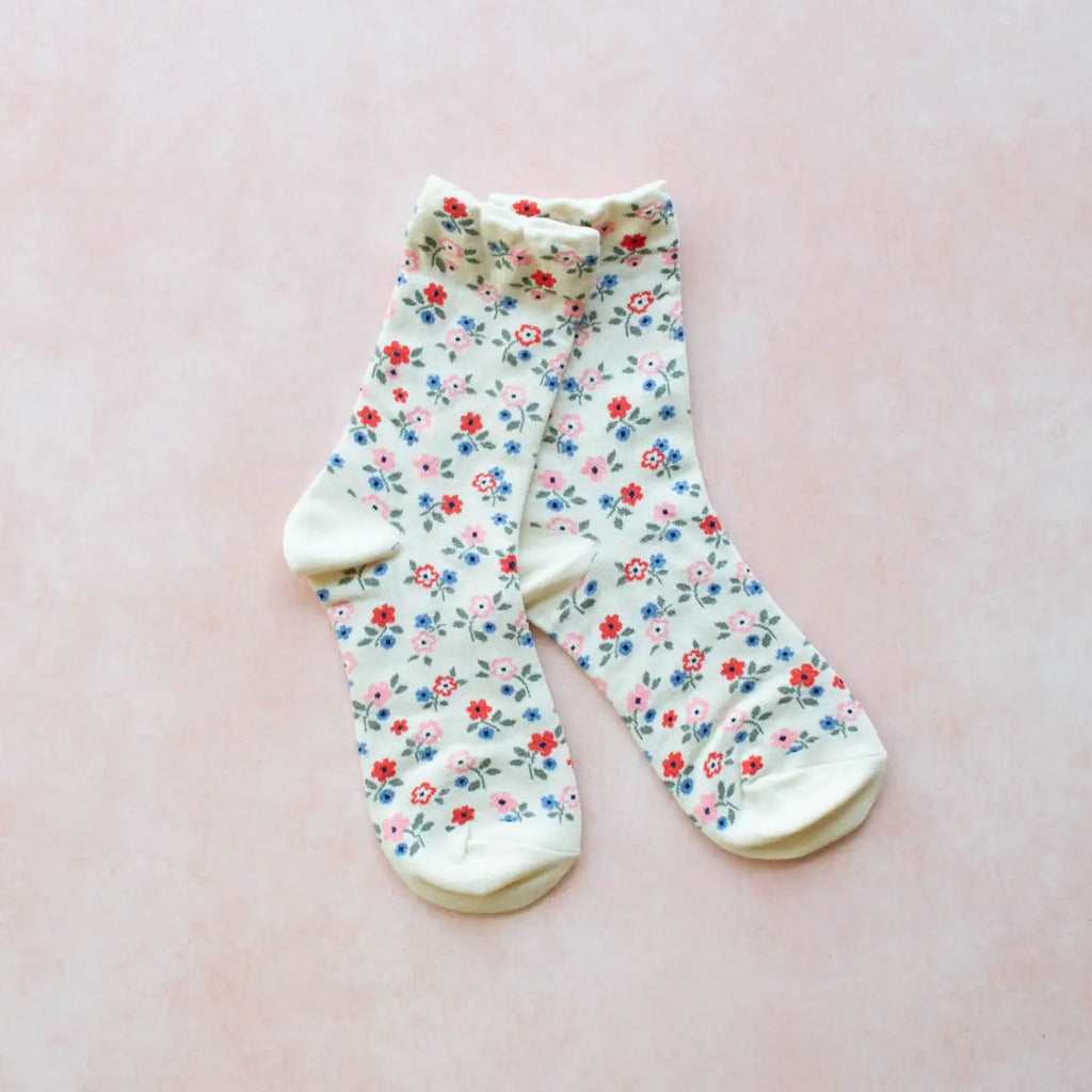 A pair of floral patterned socks laid out flat on a pink background.