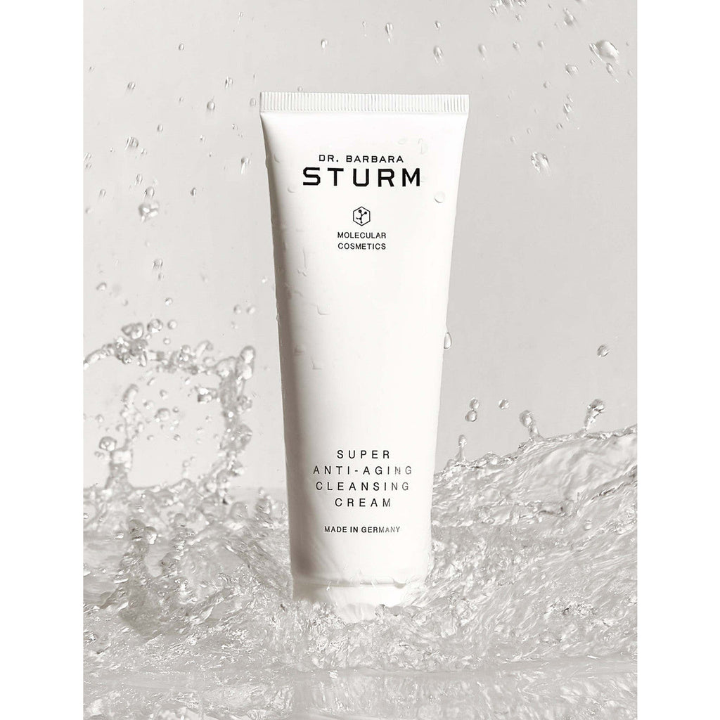 A tube of dr. barbara sturm anti-aging cleansing cream amidst splashing water.