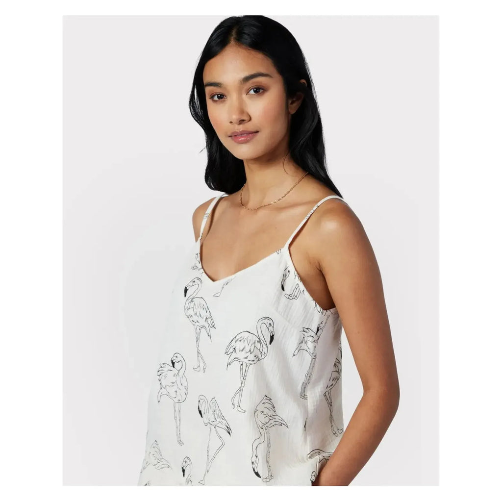 A woman with long black hair wears a white spaghetti-strap top featuring a flamingo print. She is posing against a plain light grey background, showcasing her stylish Chelsea Peers Cotton Cheesecloth Flamingo Sketch Print Cami Short Pajama Set.