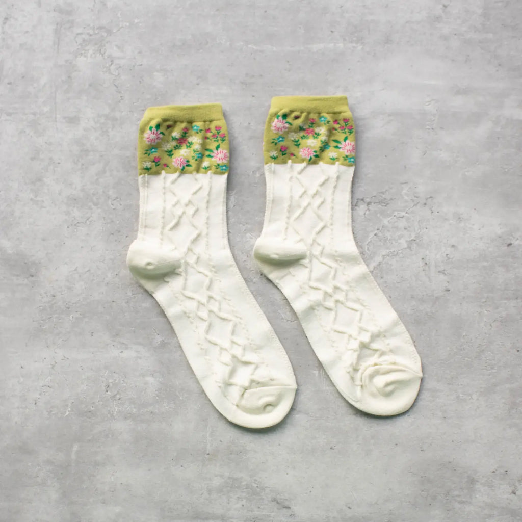 A pair of white socks with green trim and a floral pattern at the ankles on a grey background.