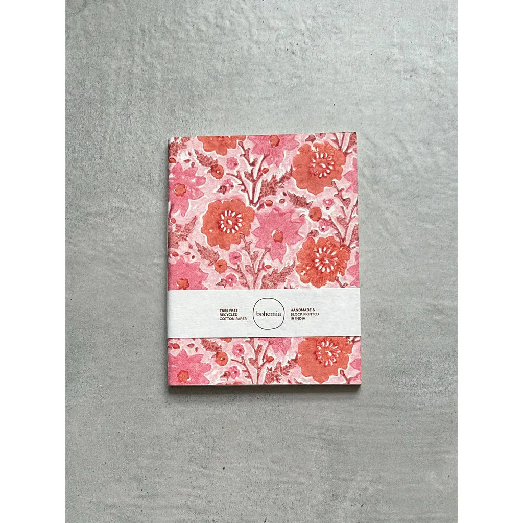 A floral patterned notebook with a pink and red design, placed on a grey background, secured with a belly band.