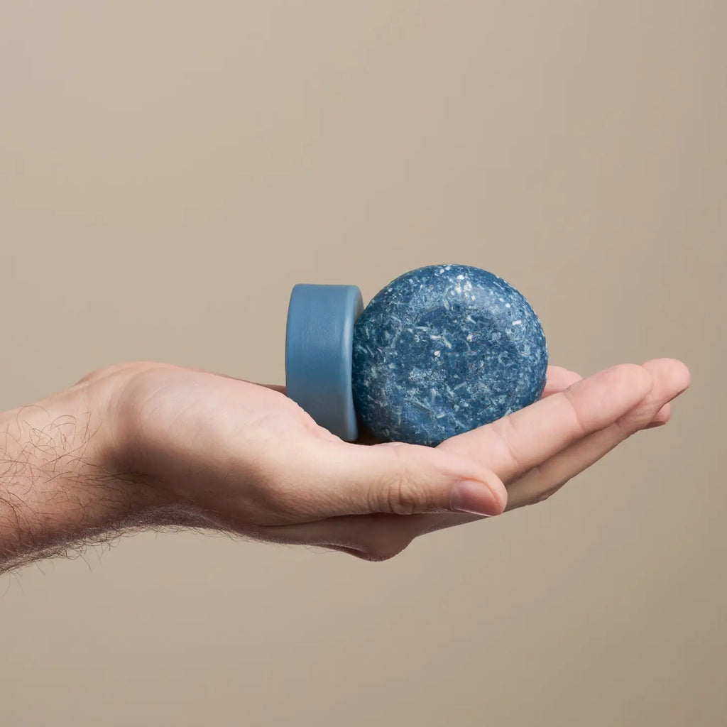 A hand holding a sphere with a blue textured surface against a neutral background.