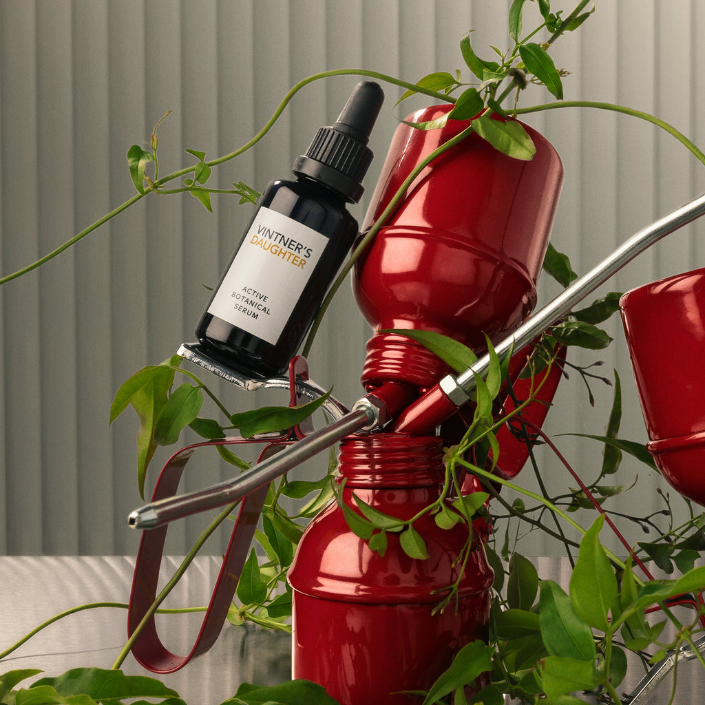 A bottle of skin care product perched on a red spiral stand with green plants.