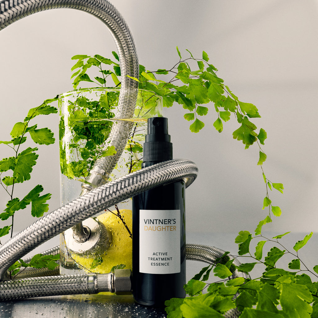 A skincare product next to a glass of water with plants and a flexible metal tube.