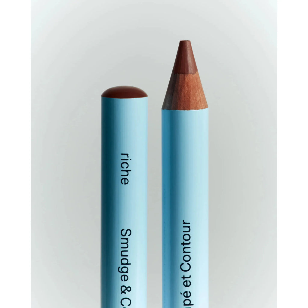Two blue cosmetic pencils, one capped and one sharpened, against a neutral background.