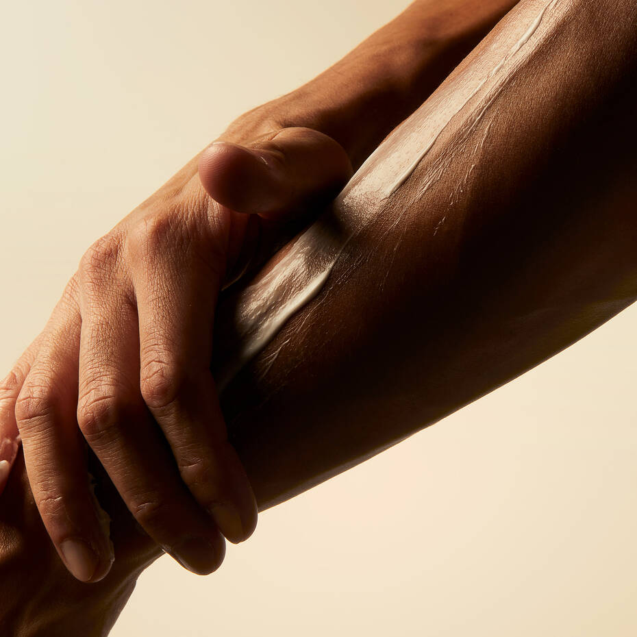 One hand applying body lotion to a forearm against a neutral background.