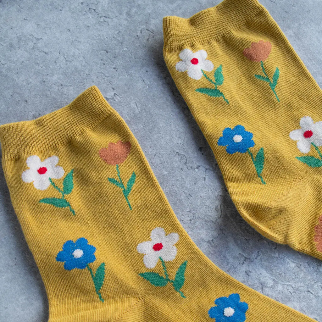 A pair of yellow socks with floral patterns on a gray textured surface.