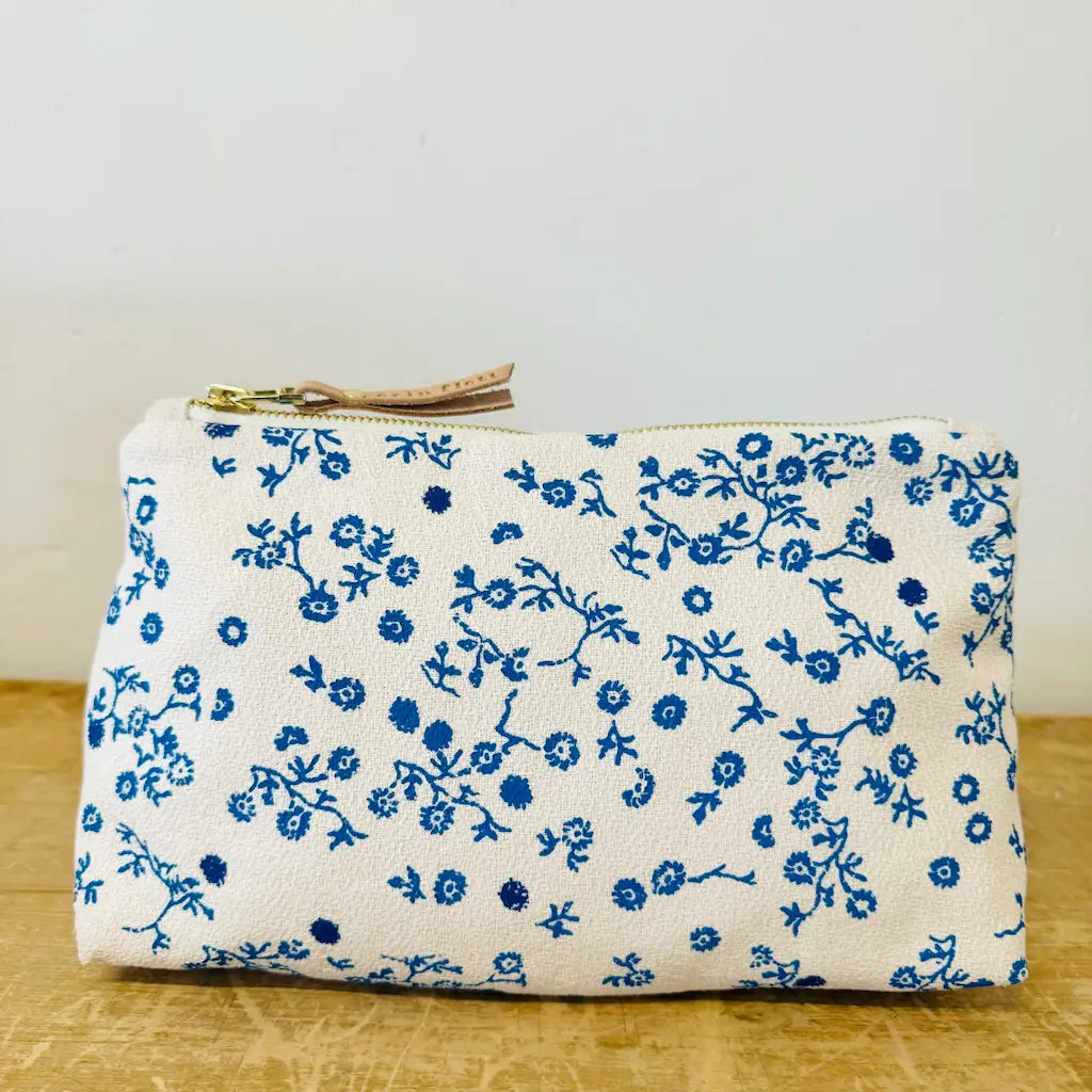 A white fabric pouch with a blue floral pattern and a zipper closure.