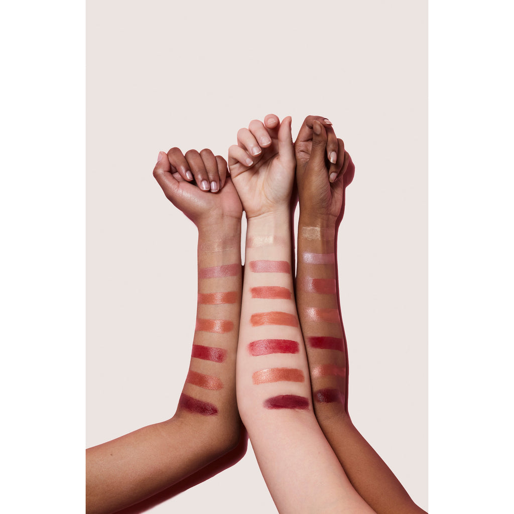 Four arms with various skin tones displaying swatches of lipstick shades.