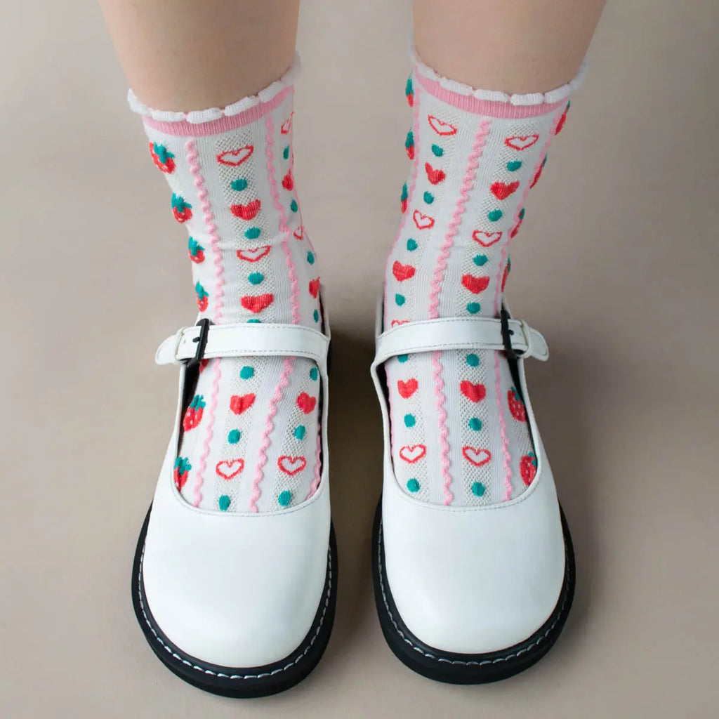 A person standing in white t-bar shoes with strawberry patterned socks.