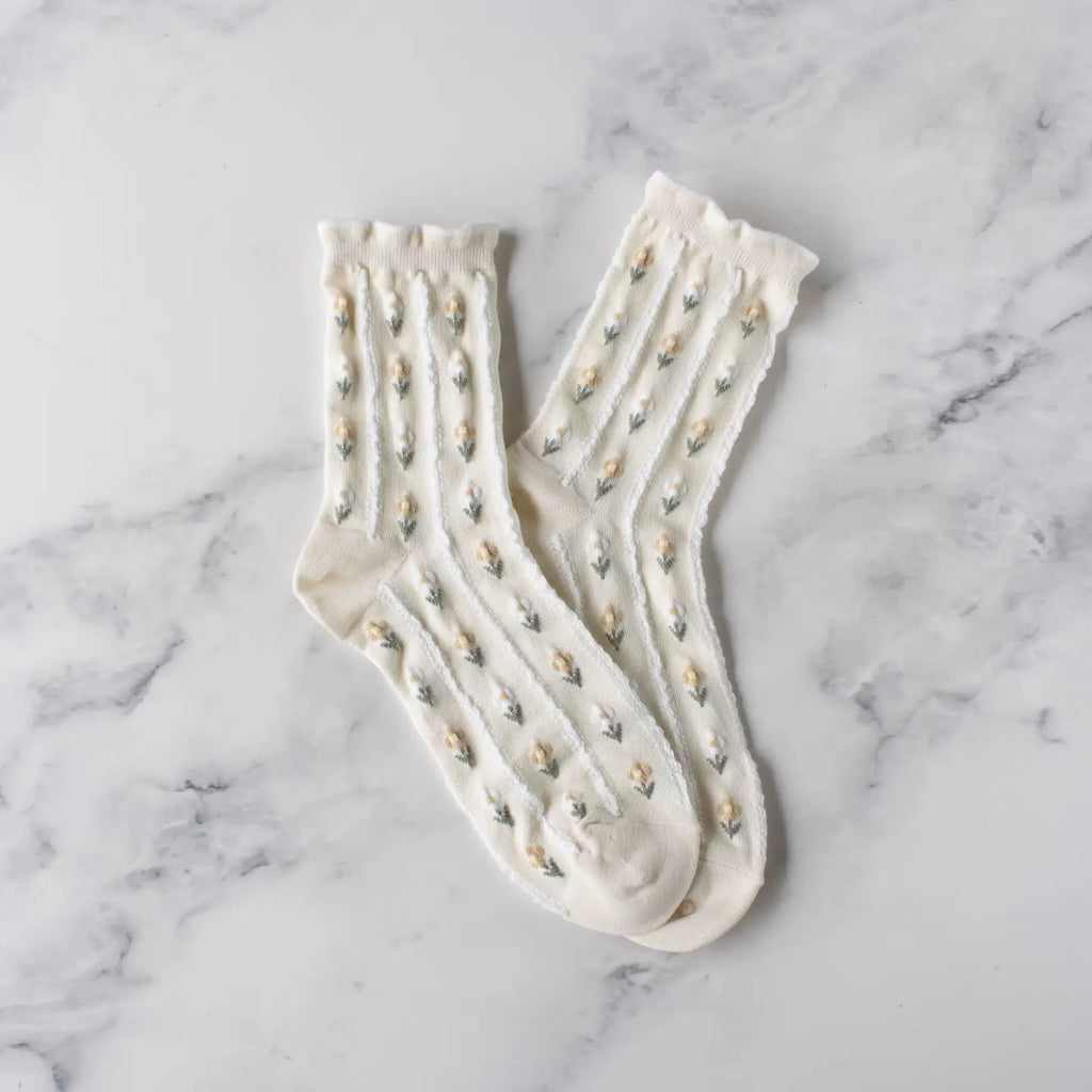 A pair of white socks with decorative patterns on a marble surface.