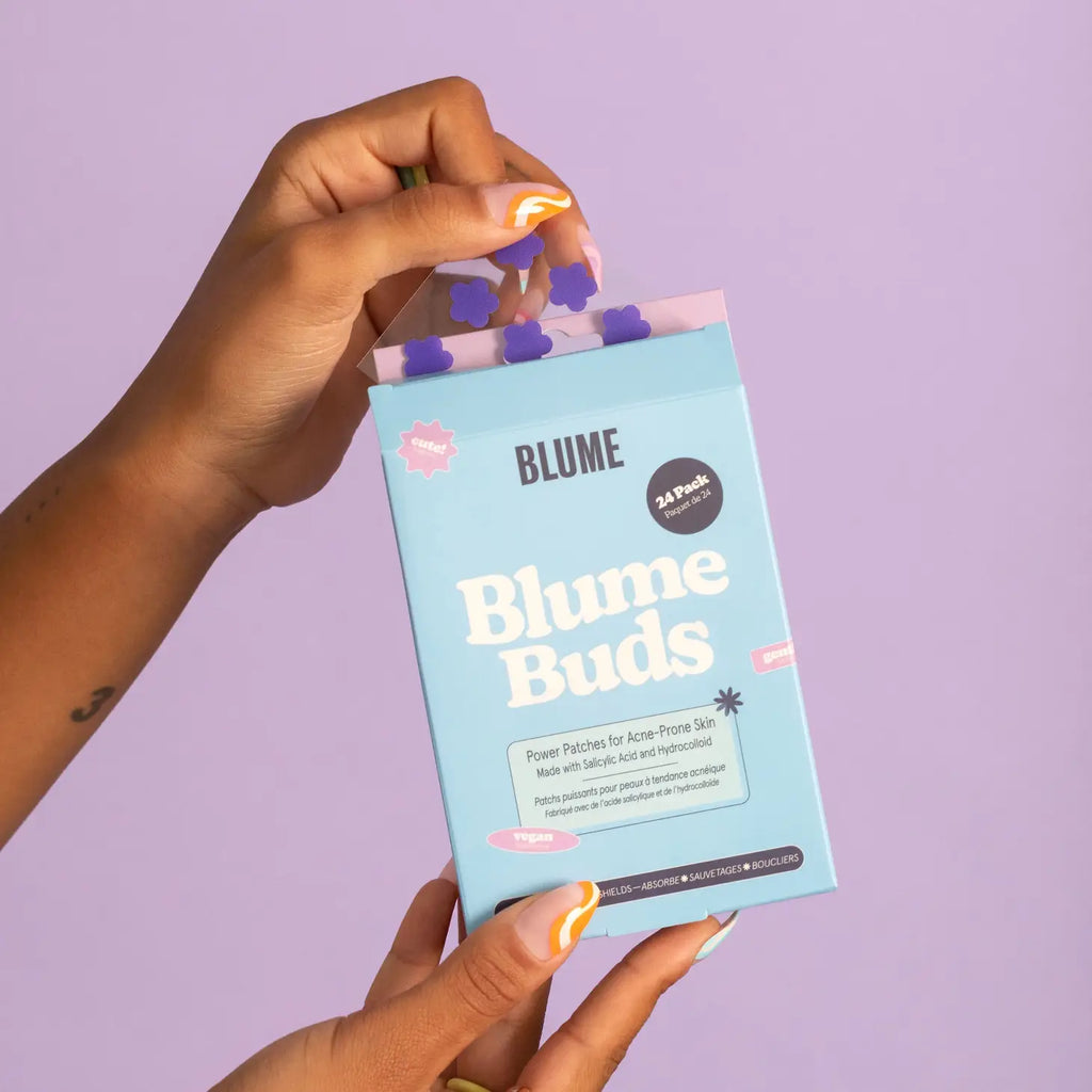 A person holding a box of blume buds acne treatment patches against a purple background.